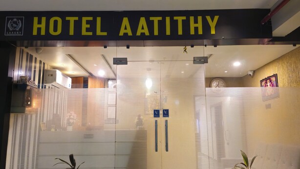 La entrada del Hotel Aatithy, con un diseño moderno, presenta una puerta de cristal grande y un letrero en la parte superior.