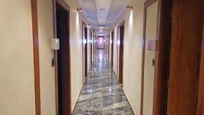 Un pasillo largo y estrecho con suelo de mármol y puertas de madera a ambos lados.