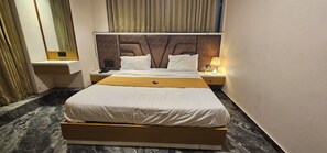A hotel room with a bed, nightstand, lamp, and curtains. - Hotel Aatithy (Ahmedabad)