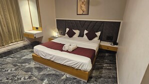 Una habitación de hotel con suelo de mármol, una cama con ropa de cama blanca y roja, cabecero con diseño geométrico, mesita de noche con lámpara y un ventanal con cortinas.