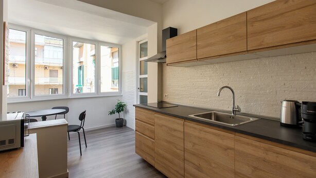 A modern kitchen with wooden cabinets, a black countertop, and a stainless steel sink. There is a window providing natural light and a view of the outside.