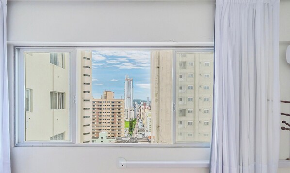 Une fenêtre donnant sur un paysage urbain, avec des gratte-ciel et un ciel dégagé.