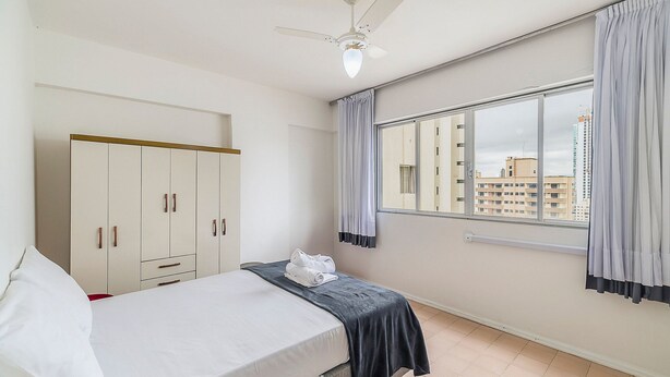 A bedroom with a bed, a wardrobe, a window with curtains, and a ceiling fan. - Well-located ap in Beachfront Condominium Iptr0171 (Balneário Camboriú)