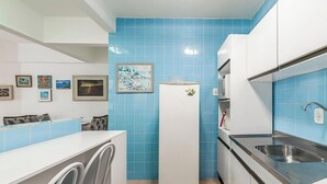 Cocina compacta con azulejos azules, un refrigerador, un microondas, un lavamanos y una lavadora.