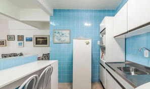 Uma cozinha compacta com azulejos azuis, geladeira, micro-ondas, pia e máquina de lavar.
