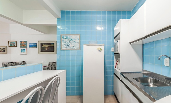 Een kleine keuken met blauwe tegels, een koelkast, een magnetron, een spoelbak en een wasmachine.
