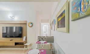 Uma sala de estar moderna com televisão de tela plana, um espaço de jantar com mesa posta para dois e um corredor com obras de arte emolduradas.