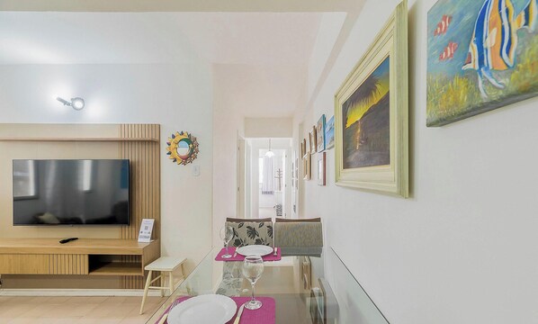 A modern living room with a flat-screen TV, a dining area with a table set for two, and a hallway with framed artwork. - Well-located ap in Beachfront Condominium Iptr0171 (Balneário Camboriú)