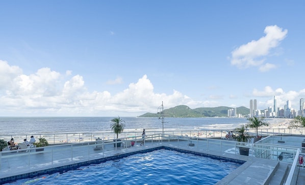 Piscina no terraço com vista para a praia e o horizonte da cidade.