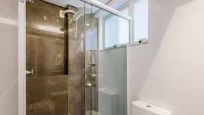 A modern bathroom with a glass shower enclosure, a toilet, and a window.