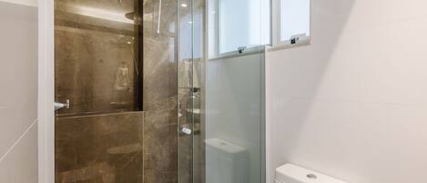 Un baño moderno con cabina de ducha de vidrio, inodoro y ventana.