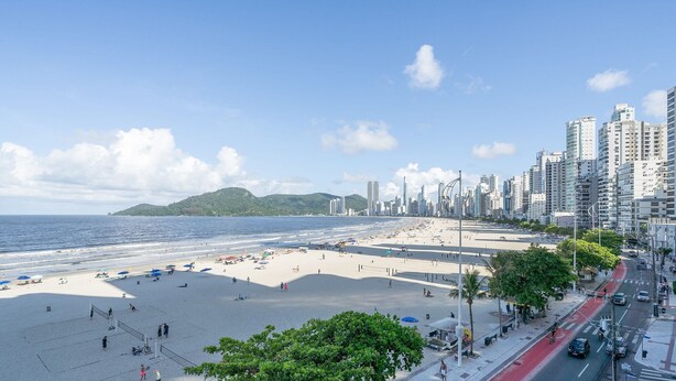 A beach with a cityscape in the background, including high-rise buildings and a hilly island.