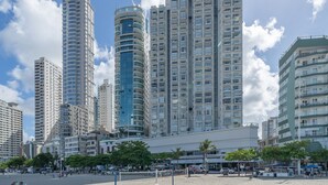 A high-rise building with multiple floors, a commercial area with shops and outdoor seating, and a sandy area with a volleyball net.
