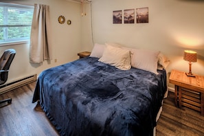 A bedroom with a bed, a chair, a nightstand, a lamp, and two wall art pieces.