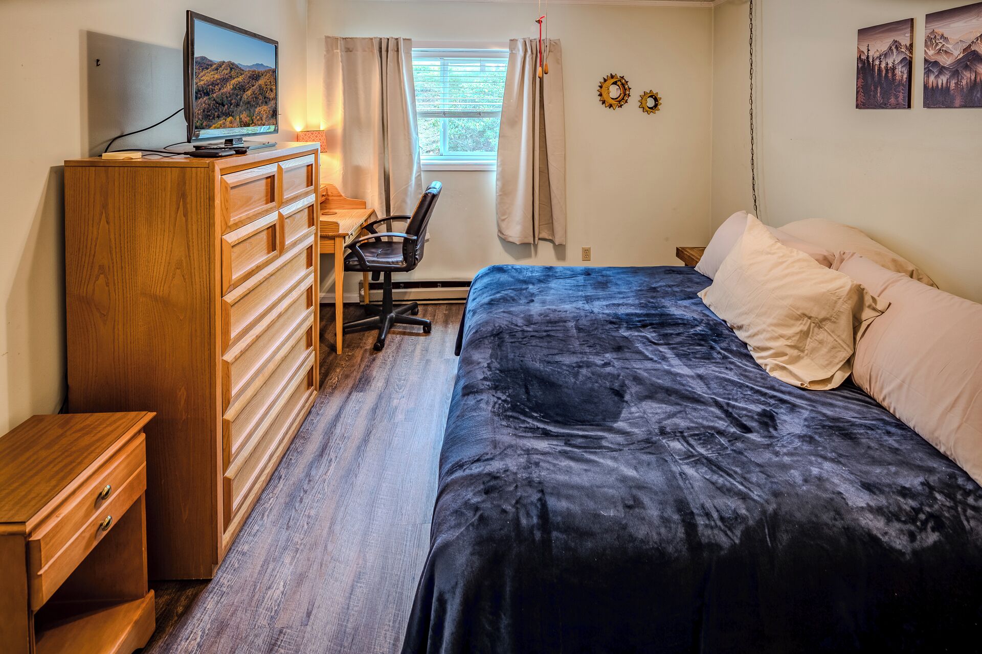 A bedroom with a bed, a desk, a chair, a dresser, and a television.