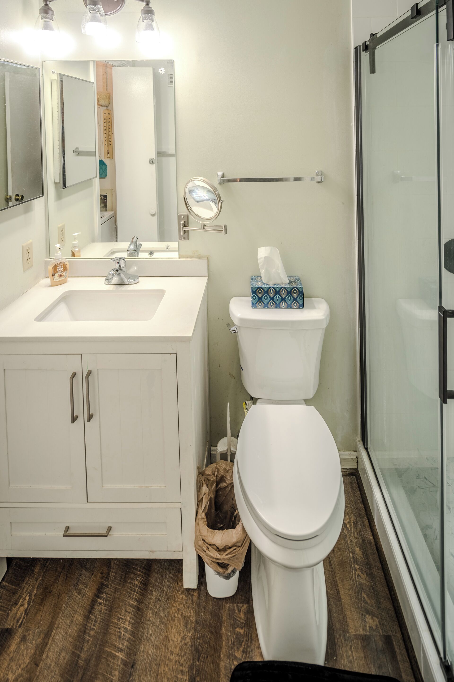 A bathroom with a white sink, mirror, and toilet. There is a shower area with glass doors.