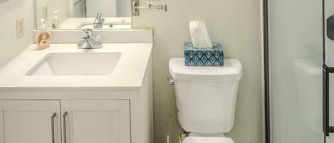 A bathroom with a white sink, mirror, and toilet. There is a shower area with glass doors.