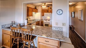A kitchen with wooden cabinets, granite countertops, a built-in microwave, and a clock on the wall. - Sugar Ski Premium Two Bedroom - Unit 825 (Sugar Mountain)