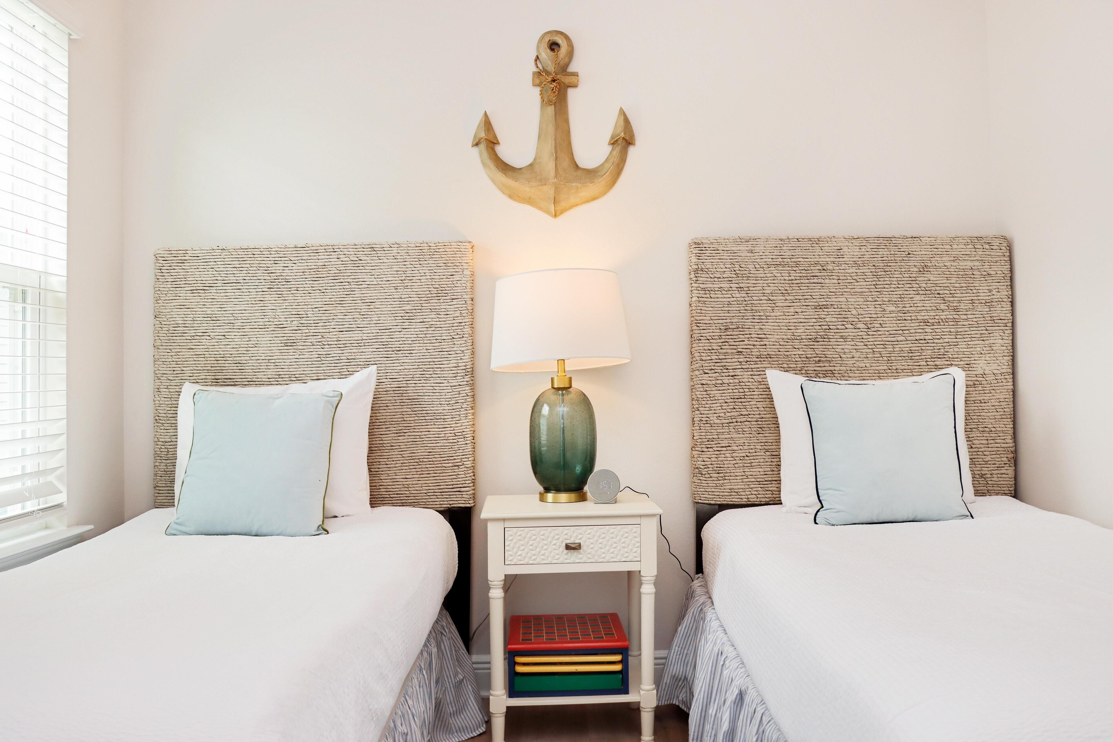 Une chambre double avec deux lits, une table de chevet avec une lampe et une ancre décorative accrochée au mur.