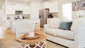 A modern kitchen with white cabinets, a central island, and a dining area. - Sunset Bliss Cove (Port St. Joe)