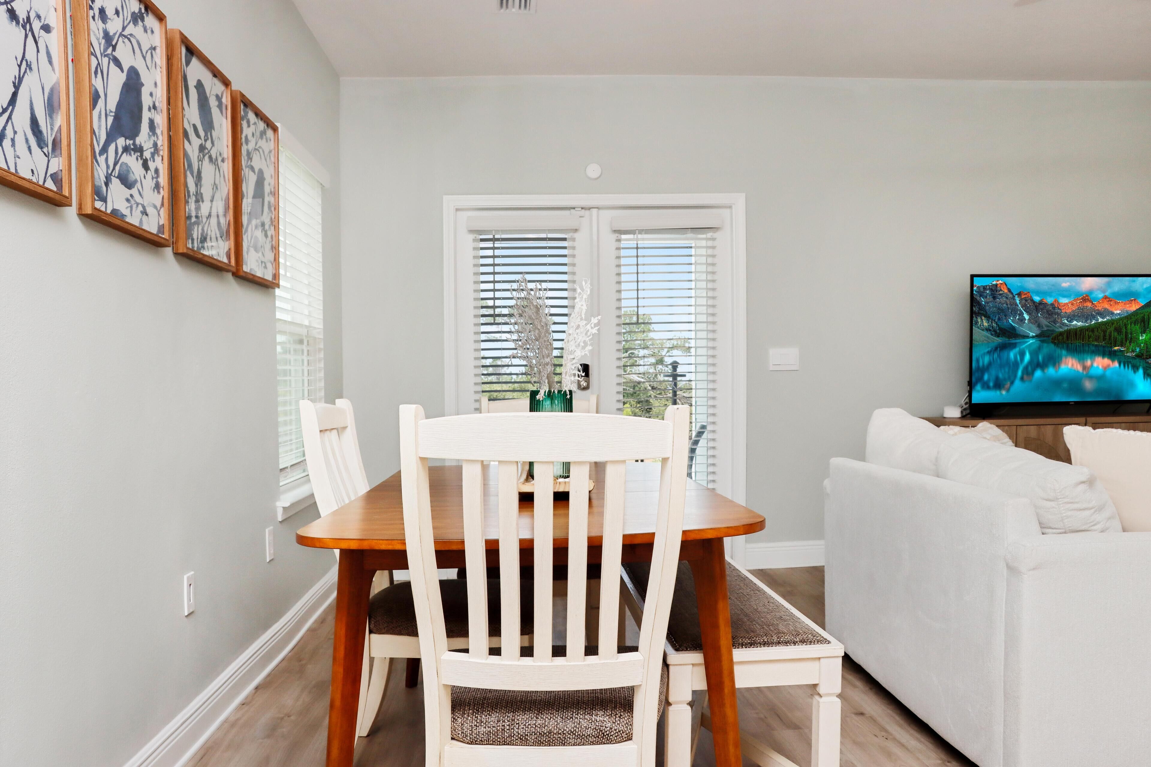 Een eethoek met een houten tafel en stoelen, een witte bank en een televisie aan de rechterkant.
