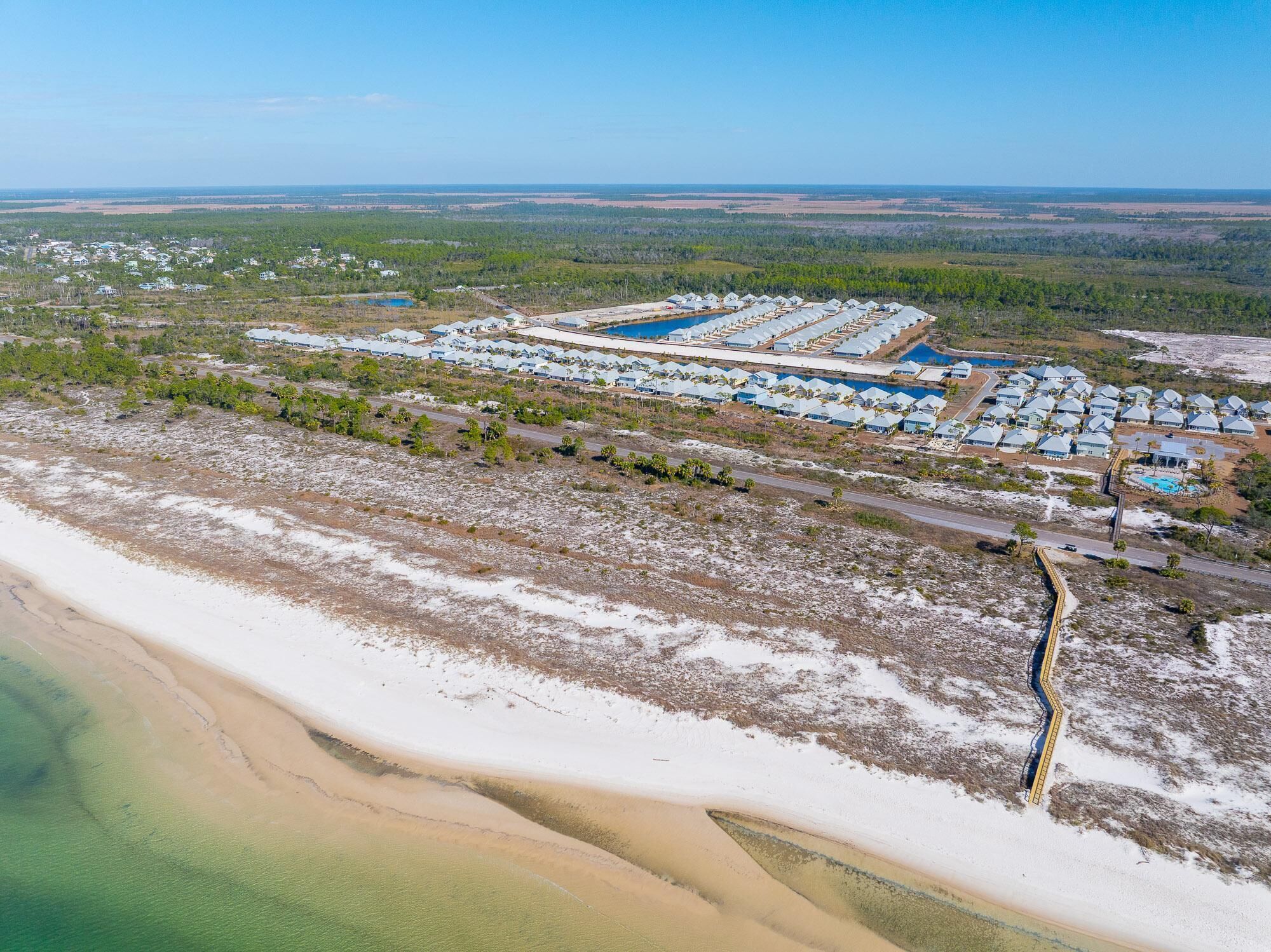 An aerial view of a coastal resort with multiple bungalow-style accommodations, a central pool, and a beach area.