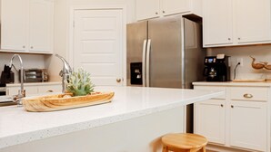 A modern kitchen with white cabinets, a stainless steel refrigerator, a coffee maker, and a wooden cutting board with food. - Sunset Bliss Cove (Port St. Joe)