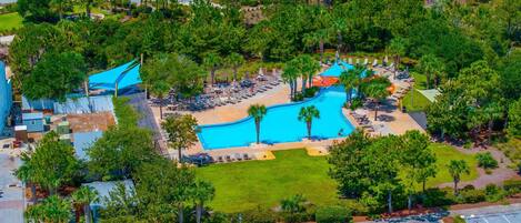 An aerial view of a resort with a swimming pool, lounge areas, and a parking lot.