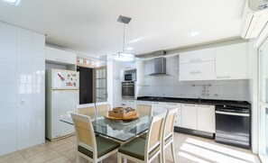 Cozinha moderna com armários brancos, uma mesa de jantar de vidro e uma lava-louças de aço inoxidável.