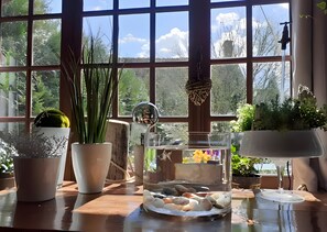 A room with large windows, a wooden table, various potted plants, a clear glass fish tank, and a white lamp.