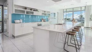 A modern kitchen with a large island, bar stools, and a view of the sky through large windows.
