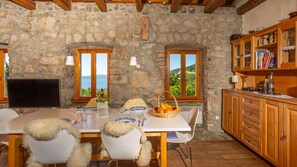 Une pièce aux murs de pierre, avec une table à manger, des chaises et une vue sur la mer.