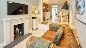 A modern living room with a fireplace, a large flat-screen TV, a leather sofa, and a dining area with a chandelier. - Host & Stay | George Street Retreat (Brighton and Hove)