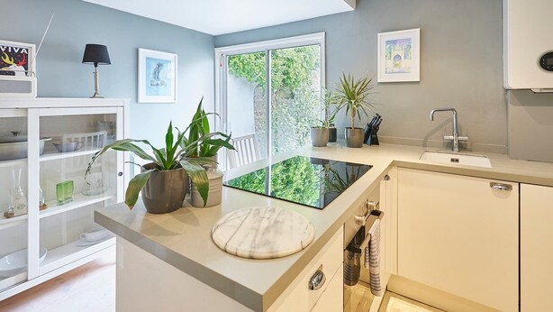 A modern kitchen with a glass-top island, white cabinetry, and a view of greenery through large windows. - Host & Stay | George Street Retreat (Brighton and Hove)