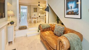 A living room with a leather sofa, a dining table, and chairs. There is a staircase leading to an upper floor. - Host & Stay | George Street Retreat (Brighton and Hove)