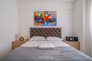 A modern hotel room with a tufted headboard, a bed with grey bedding, two white pillows, a bedside table with a lamp and a radio, and a colorful abstract painting on the wall. - Apt w/ Balcony & BBQ 400m From Beach Dbr0805 (Itapema)