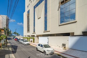 A street view with a row of parked cars and a building with large windows and a white facade. - Apt w/ Balcony & BBQ 400m From Beach Dbr0805 (Itapema)