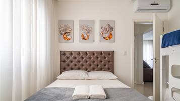 A neatly arranged hotel room with a tufted headboard, a bed with white linens, and three abstract paintings on the wall.