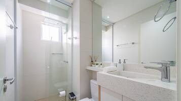 A modern bathroom with a glass shower enclosure, a white sink with a mirror, and a toilet.
