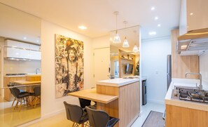 Una cocina moderna con una isla central, un comedor con sillas y un cuadro abstracto grande en la pared.