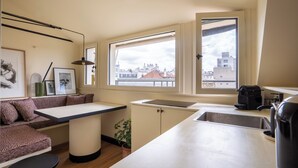 A compact kitchen with a built-in sink, a dining area with a bench, and a view of the city through large windows. - Luxurious, quiet, bright studio in the heart of the south of Pigalle (Paris)