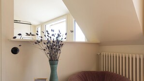 A room with a white ceiling, a window, a radiator, a round table with a vase and a framed picture, and a purple chair. - Luxurious, quiet, bright studio in the heart of the south of Pigalle (Paris)