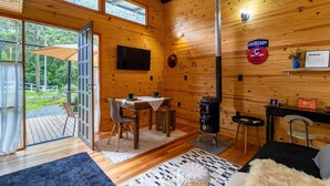 A wooden cabin interior with a dining area, a fireplace, and a large window overlooking a garden.
