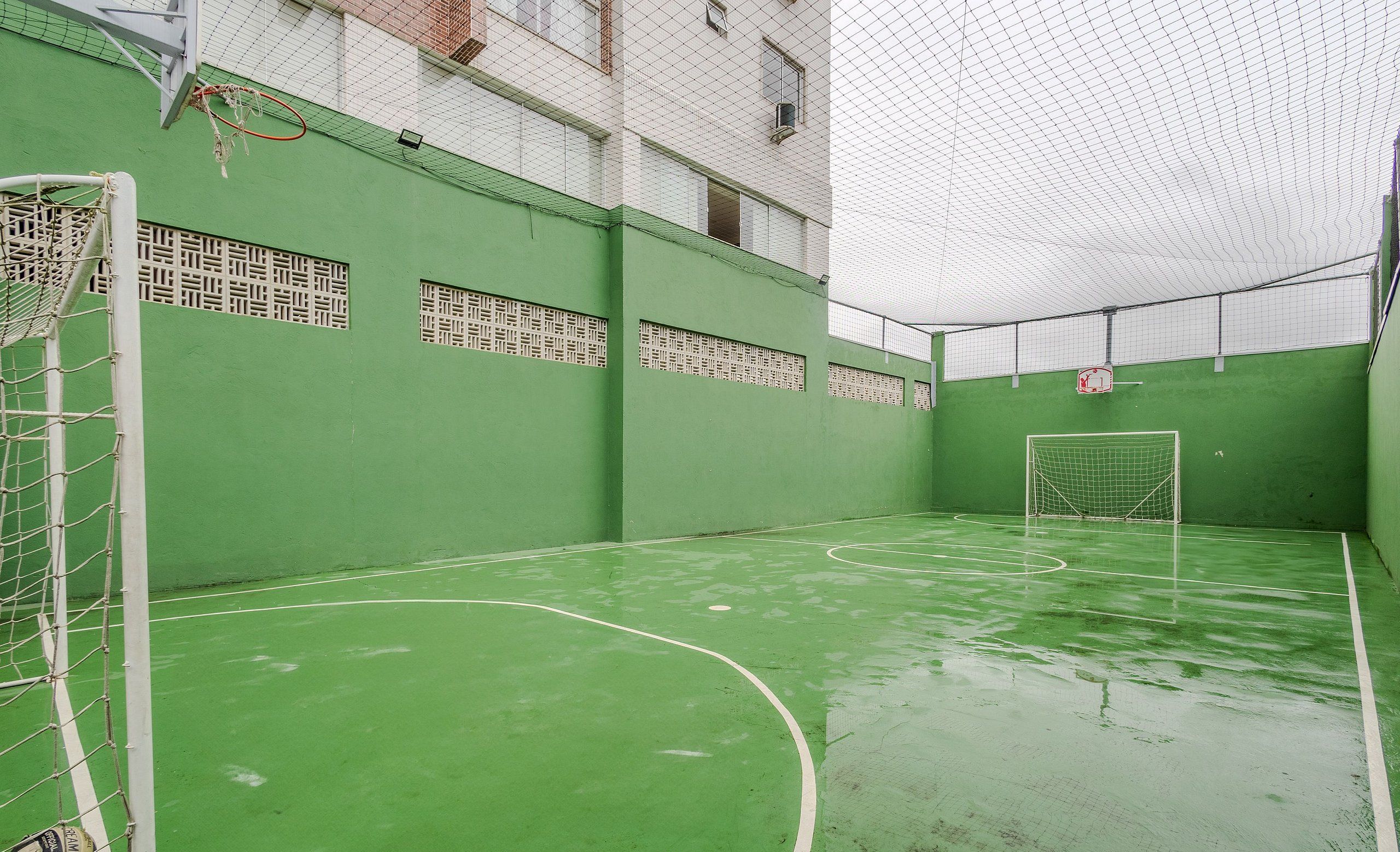 Een binnensportveld met groene vloer en witte lijnen, een doelpunt en een net.