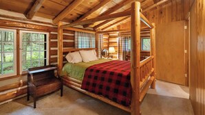 Een slaapkamer in een blokhut met een hemelbed, een houten bankje en grote ramen met uitzicht op het bos.