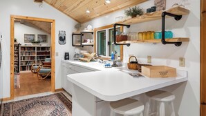 Een moderne keuken met witte aanrechtbladen, houten planken en een groot eiland met barstoelen.