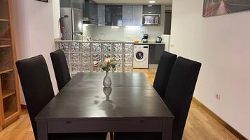 Una mesa de comedor con sillas, un florero con flores, un reloj y una cocina al fondo.