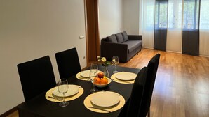 A dining area with a table set for four, a sofa, and a large window with curtains. - Bright Two-Bedroom Apartment in Maragall (Barcelona)