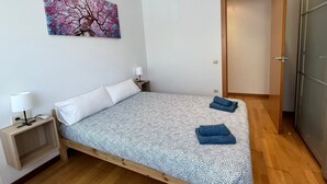 A single bed with a patterned bedspread, a bedside table with a lamp, a wall-mounted air conditioner, and a door to the right. - Bright Two-Bedroom Apartment in Maragall (Barcelona)