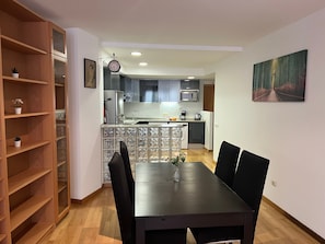 A modern kitchen with a dining area, wooden shelving, and a clock. - Bright Two-Bedroom Apartment in Maragall (Barcelona)